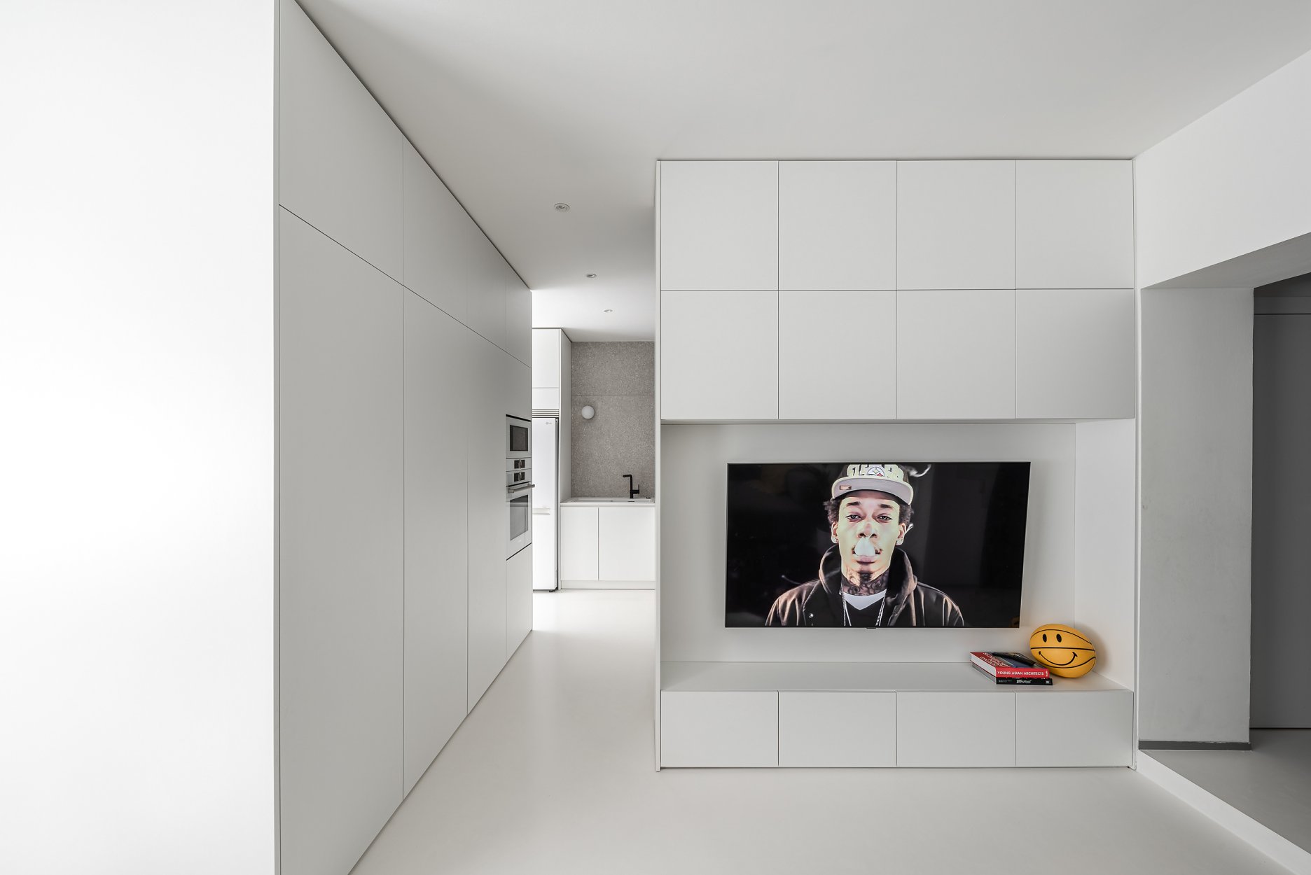 Abstrakcia výrazu: obývacia izba je vymedzená nábytkom vyrobeným na mieru – televíznou stenou, ktorá čiastočne prekrýva kuchynskú linku. Dizajn vstavaného nábytku je zredukovaný na estetiku krajného minimalizmu.