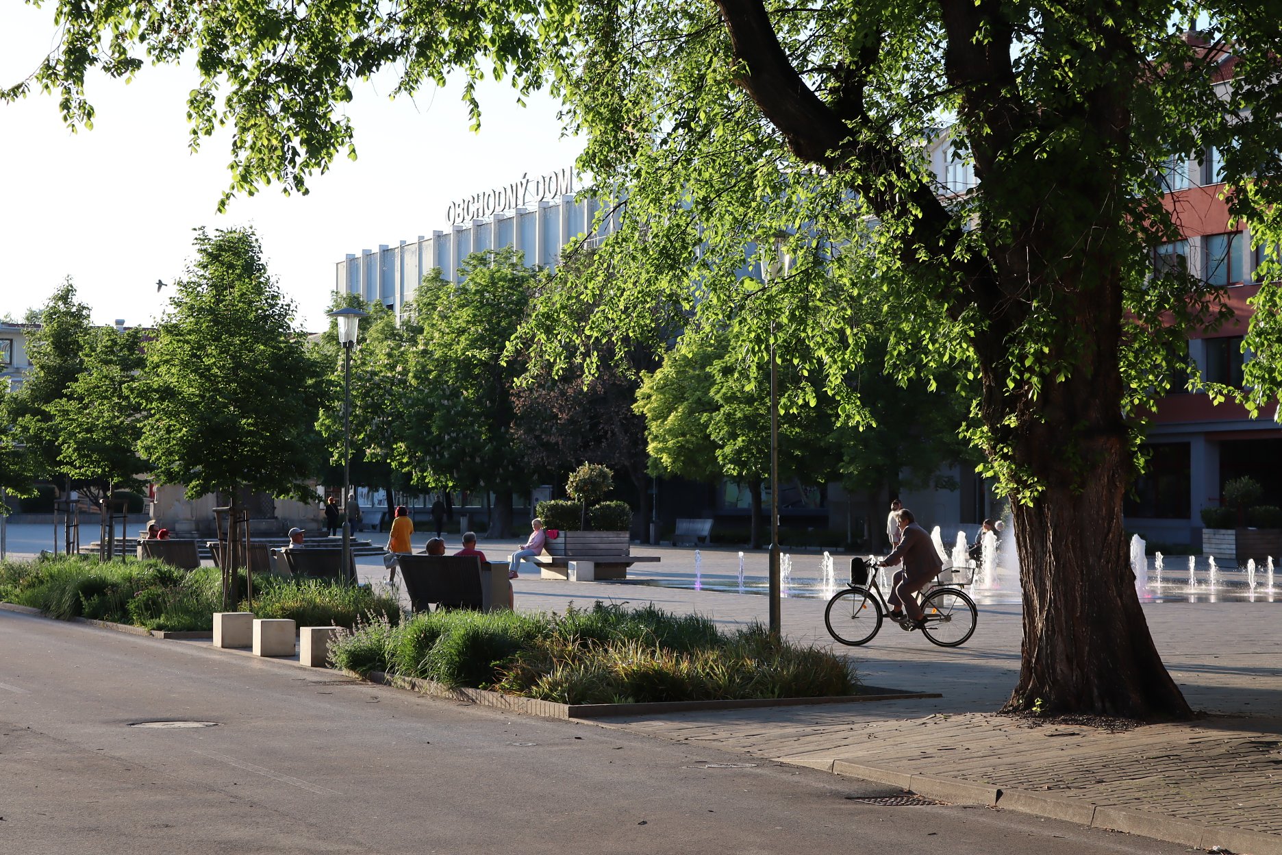 Pohľad na Hlavné námestie z Komárňanskej ulice. Projekt obnovy integroval všetky existujúce dreviny a námestie ozelenil novými vodozádržnými záhonmi a výsadbami stromov a krov.